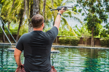 A sympathetic man launches a drone for flight, with which you can take photos and videos, near the swimming pool, view back.