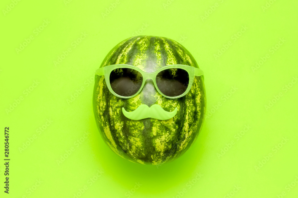 Summer funny watermelon in green glasses and with green mustache on bright green background top view flat lay. Minimal fruit concept. Creative product idea, summer festival, summer background - obrazy, fototapety, plakaty 