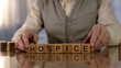 Grandfather making word hospice of wooden cubes on table, elder care, disorder