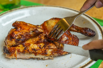 People using knife cutting grilled chicken leg on white plate