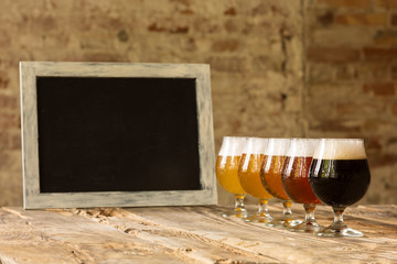 Glasses of different kinds of dark and light beer on wooden table in line. Cold delicious drinks prepared for a big friend's party. Concept of drinks, fun, meeting, oktoberfest. Copyspace.