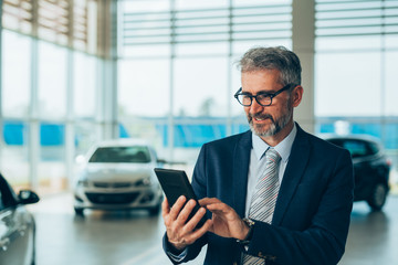 senior agent using cellphone in car dealership showroom