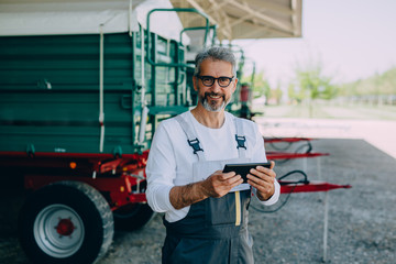 worker using tablet standing by agricultural machinery