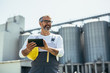 © cherryandbees - engineer using tablet in front of blurred grain silos