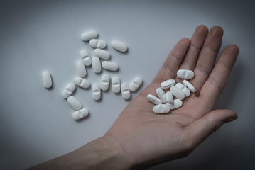 Hand holding many white prescription drugs, medicine tablets or vitamin pills in a pile - Concept of healthcare, opioids addiction, medicament abuse or medication treatment