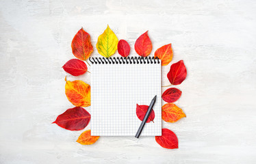 Paper Notepad, pencil and bright autumn red and yellow leaves on white table. white notebook decorated autumn leaves on table. Autumn composition, fall time season. Top view. copy space