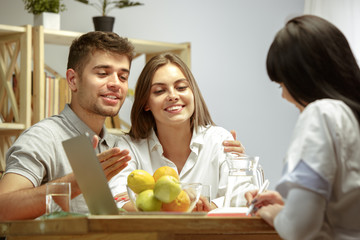 Smiling nutritionist showing a healthy diet plan and fruits to patient. Young couple visiting a doctor for having a nutrition recommendations. Healthy lifestyle and food, medicine and treatment.