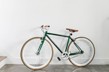 Fixed Green And Brown Bicycle In Modern Home, Fixie Bike Inside Hous​e, White Wall Background, Isolated Retro Bicycle 