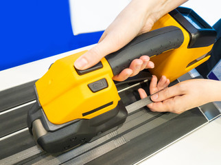 Poster - Equipment for packaging. Manual strapping machine. Girl packing goods. Technology of packaging of finished products with belts.