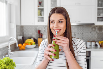 Wall Mural - Happy woman drinking green juice or shake at home