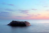 Fototapeta Psy - A stone in a calm sea at sunset