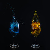 Fototapeta Paryż - Glasses with blue and yellow water on a black background. Splashing water. Additional colors.