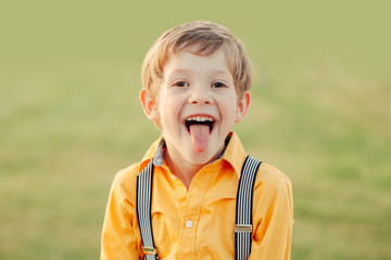 Closeup portrait of funny blond Caucasian preschool boy making faces in front of camera. Child showing tongue against plain light green background. Kid expressing emotions.