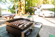Bacon And Sausage Cooking On A Camp Grill