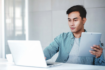 Happy Young Businessman Working on Computer Laptop and Digital Tablet in Office