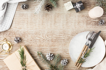 Festive wooden table setting with winter decorations, cutlery, candles and gifts. Top view, flat lay. The concept of a Christmas family dinner.
