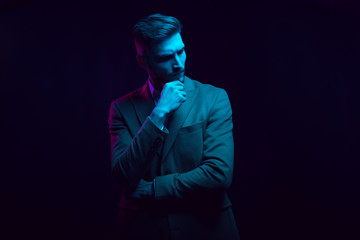 Young handsome model posing in a studio in a trendy neon light. Fashionable man in a stylish suit. Vibrant color. Bright colorful light effects. Disco style. Overlay. Gel filter. Supersaturated