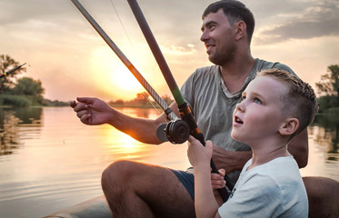 Happy Father and Son together fishing from a boat at sunset time