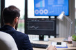 © DC Studio - Back view of young entrepreneur analysing the data from computer monitor in his office