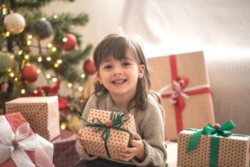 Pretty little girl is holding a gift box and smiling while sitting on her bed in her room at home