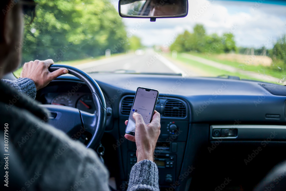 A man use smartphone while driving in the car. Road danger concept - obrazy, fototapety, plakaty 