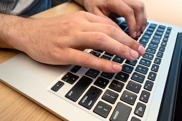 laptop computer on wood table with young man typing one the computer keys