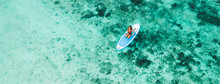 Woman Sitting On Sup Board And Enjoying Turquoise Transparent Water And Coral Reef. Tropical Travel, Wanderlust And Water Activity Concept.