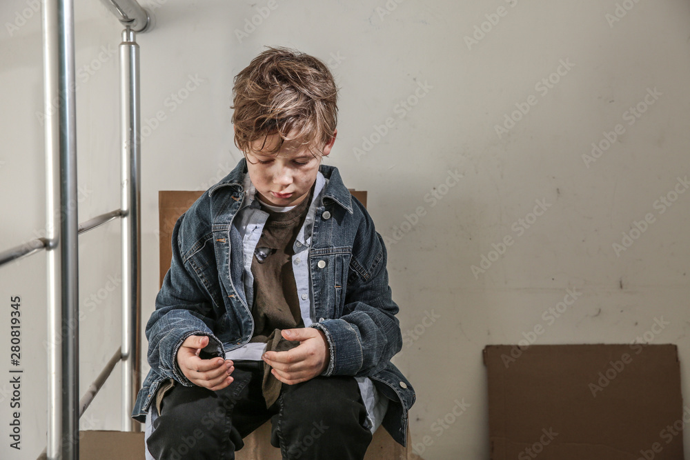 Homeless little boy sitting indoors