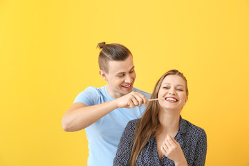 Happy man helping his girlfriend to clean teeth against color background