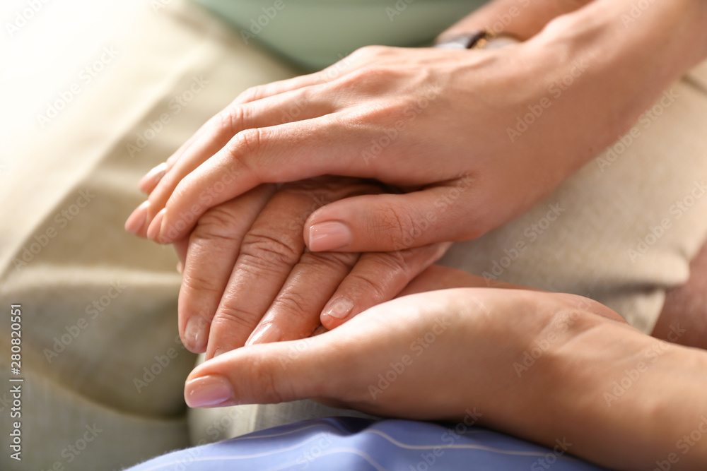 Young daughter supporting elderly mother at home, closeup