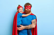 Serious tired dad entertains child on party, pretend being superheroes, have extraordinary power, play together. Little girl in blue t shirt, red cape hugs father has happy look. Family time concept