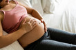 © InfiniteFlow - Pregnant woman feeling happy at home while taking care of her child. The young expecting mother holding baby in pregnant belly. Maternity prenatal care and woman pregnancy concept.