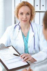 Wall Mural - Happy blonde female doctor and patient discussing medical examination results. Medicine, healthcare and help concept