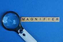 Black White Magnifier From The Word Of Wooden Letters On A Blue Table