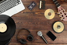 Frame From Musical Technologies On Wooden Background. Laptop, Vinyl Record, Headphones, Microphone, Smartphone, Compact Discs, Guitar And Audio Cassettes On Wooden Background.