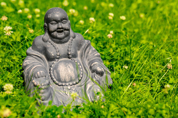 Figure of a Buddha sitting in the garden amid blooming clover.