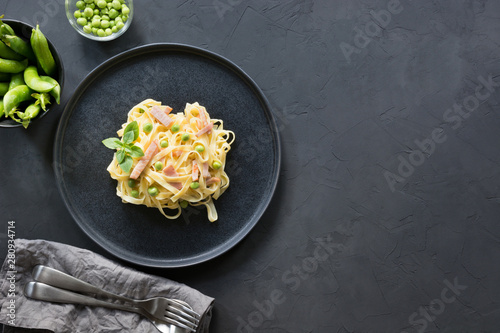 Fotografía Pasta tagliatelle with cream, peas and bacon on black background