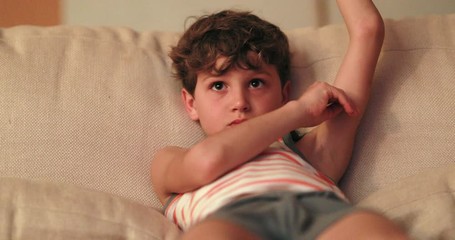 Wall Mural - Young boy seated in living-room sofa watching TV screen