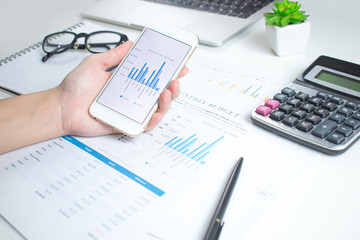 Poster - Businessmen use smartphones to calculate financial graphs on a white table.