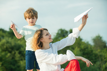 Wall Mural - Mothers day. Happy mother and little son playing on blue summer sky. Happy family - mother and child on meadow with a toy paper airplane in the summer on the nature background.