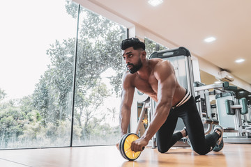 Athlete sporty man doing exercise with abs roller wheel to strengthen his abdominal muscle in gym.