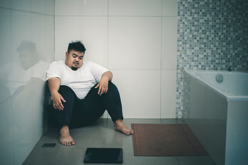 Wall Mural - Unhappy fat man sits with a scale in the bathroom
