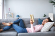 © BestForYou - Smiling woman with a book lying on the sofa in the living room.