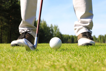 Golf player at the putting green hitting ball into a hole.