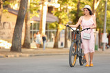 Fototapeta Miasto - Beautiful young woman with bicycle outdoors
