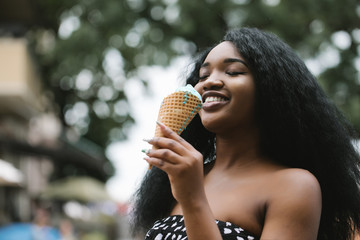 Wall Mural - Portrait of a beautiful African american woman eating one ice cream in the street.