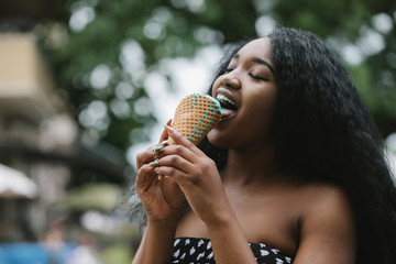 Wall Mural - Portrait of a beautiful African american woman eating one ice cream in the street.