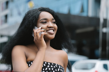 Wall Mural - Shot of a happy young businesswoman using her mobile phone while talking with somebody in front of the business center in the city.