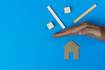 Wall Mural - Home insurance concepts. House protect. A man hand protected a small house from wooden block on blue background.