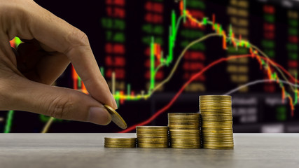 Stock market or business and finance concept. A business man hand holding coin over stack of coins with stock or forex graph. Depicts financial investment.